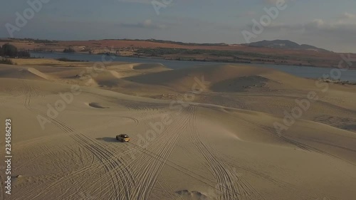 2K Aerial view. Yellow jeep drives through the desert at sunset