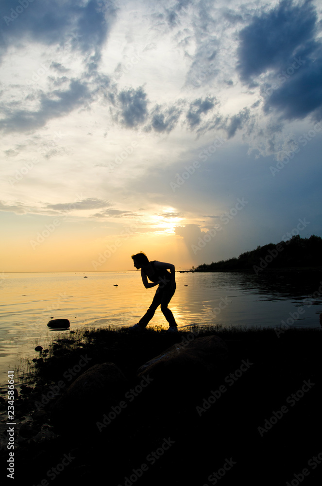 woman throws a stone into the water at sunset curving for a good throw