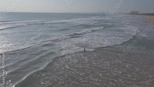 2K Aerial view of young girl in swimsuit walking on the lonely sandy beach directly into ocean at sunrise. Travel aerial footage