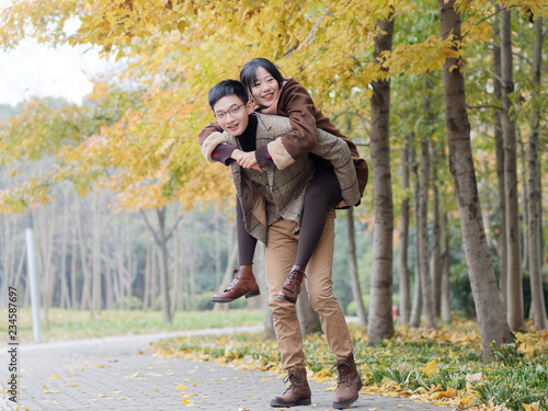 Portrait of smiling young girlfriend piggyback boyfriend during romantic walk in autumn park alley, excited couple looking at camera have fun outdoors, playing foolish, man carry lover on his back. © atiger