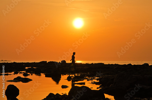 silhouette of a woman walking on a rocky beach at sunset-an evening walk along the summer shore