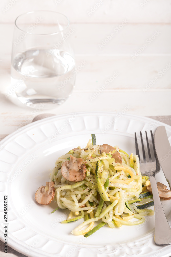 Plate of spaghetti prepared from zucchini and mushroom sauce on wooden table Plate of spaghetti prepared from zucchini and mushroom sauce on wooden table