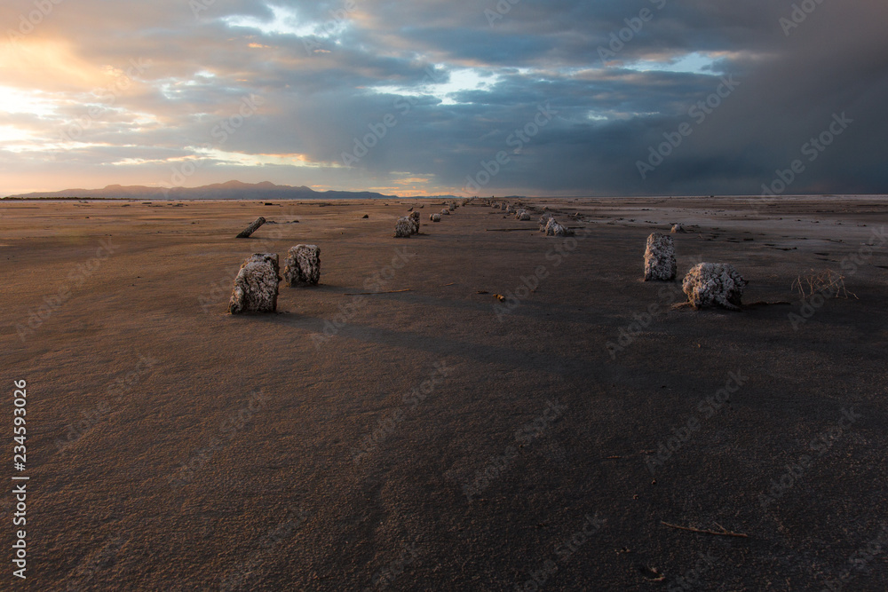 A dried-up lakebed at sunset with remnants of wood pylons coming out of the ground