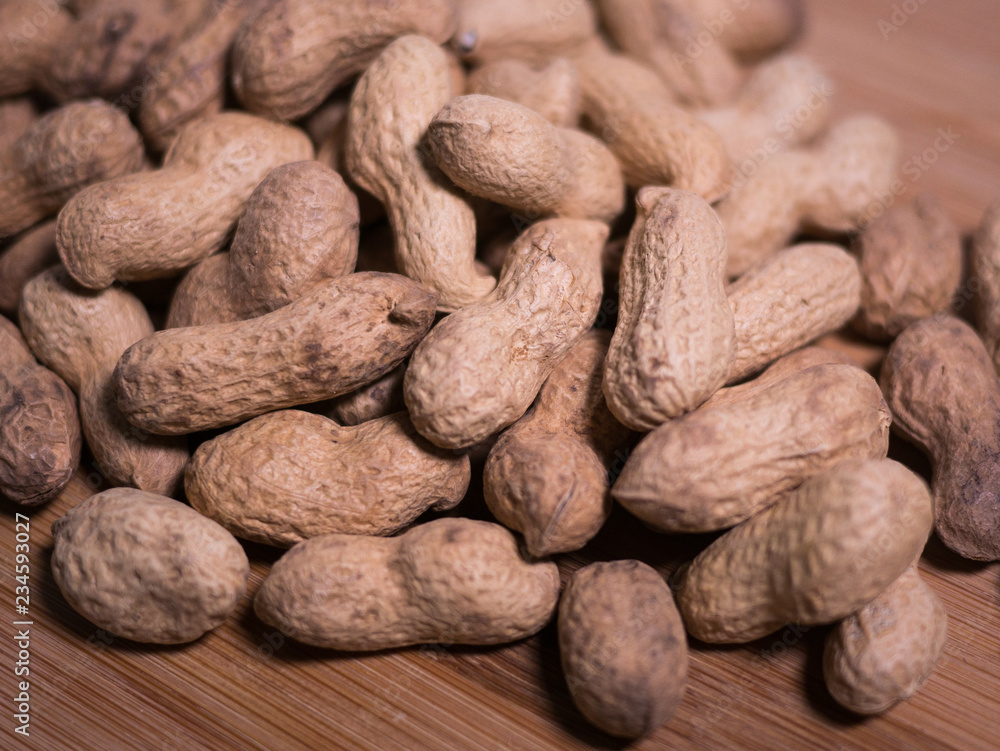Pile of unshelled whole roasted peanuts on a natural wooden surface table with shallow focus / depth of field. Pile of unshelled whole roasted peanuts on a natural wooden surface table with shallow focus / depth of field.