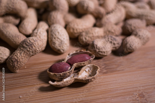 Pile of unshelled whole peanuts with one opened peanut in the foreground on a natural wooden surface table. © Barry