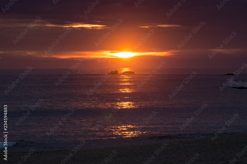 Beautiful vivid scene of summer sun setting between two rocks on the Atlantic coast of northern Portugal.