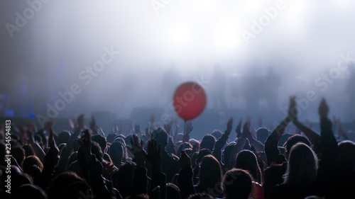 Crowd of young people in silhouette during music concert with red balloon centre frame