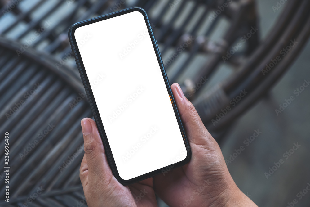 Mockup image of hands holding black mobile phone with blank white screen in outdoor