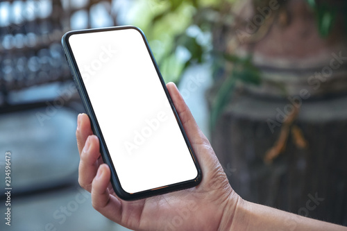 Mockup image of hand holding black mobile phone with blank white screen in outdoor