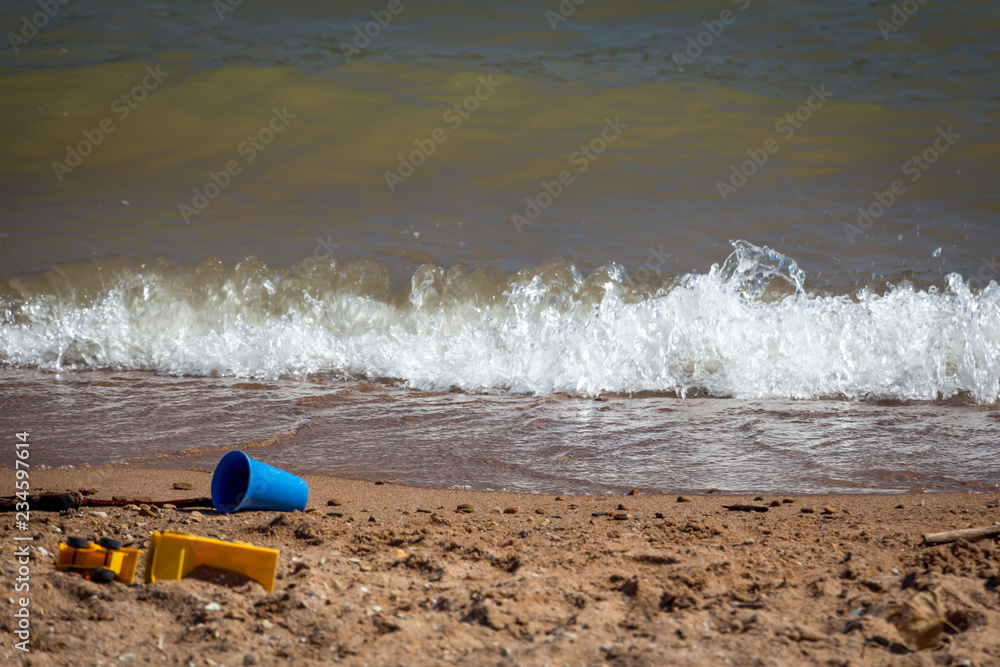 A blue pail and other toys in the sand at the beach
