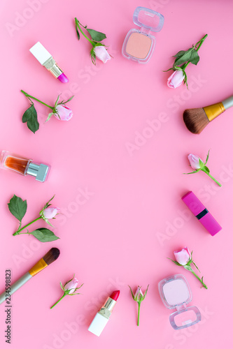 Rose, pink decorative cosmetics frame. Lipstick, bulk, eyeshadow and small rose flowers on pink background top view copy space