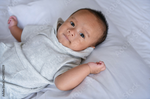 Newborn Concept. Mother and child on a white bed. Mom and baby boy playing in bedroom. Parent and little kid relaxing at home. Family having fun together. Newborn baby is fussing and crying.