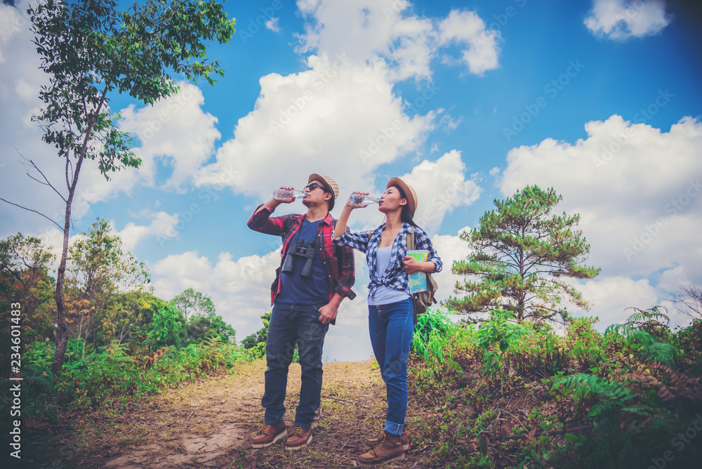 Young couple hiking tourist with backpack drinking water in nature.