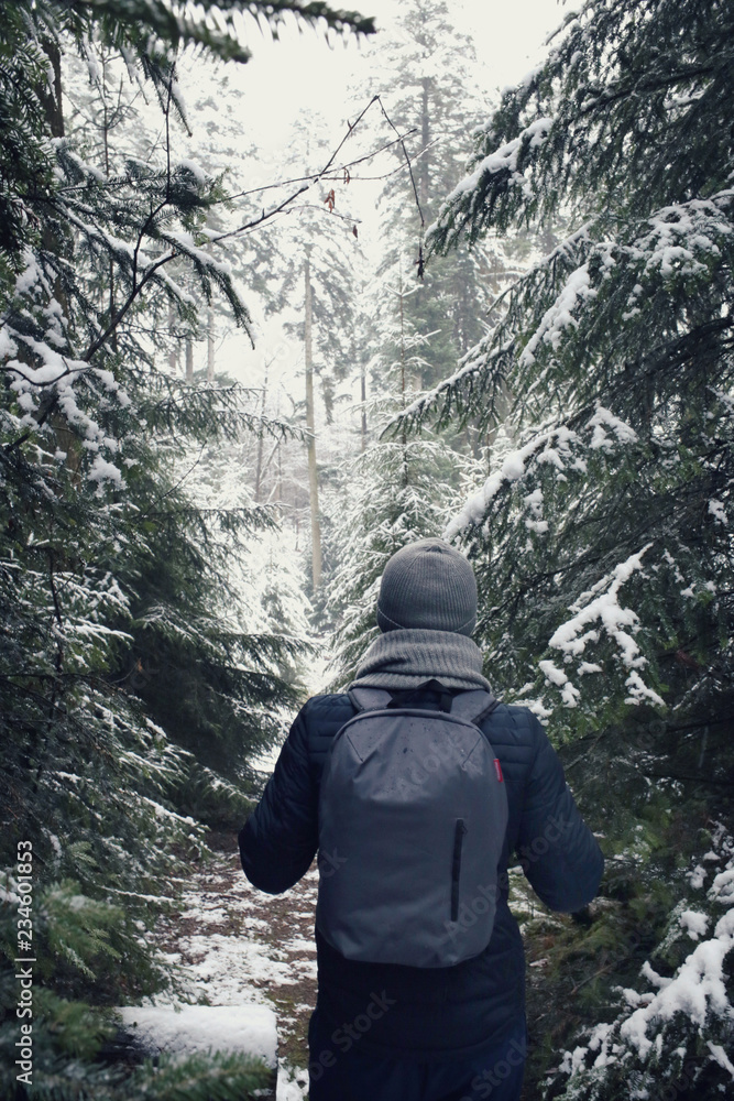 Winter tourism. winter walk.Male traveler with a backpack in the fir snow forest. Man on a winter forest road