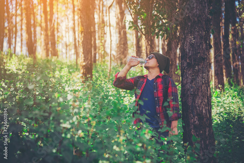 Happy hipster man tourist with backpack drinking water while hiking in nature forest.