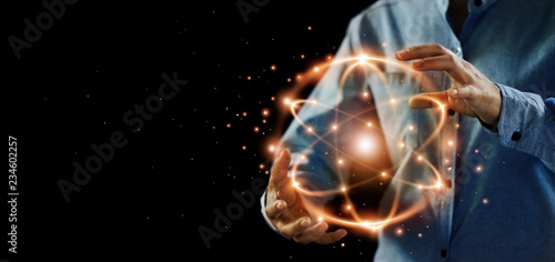Abstract science, hands holding atomic particle, nuclear energy imagery and network connection on dark background.