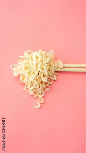 Instant noodles and chopsticks on a pink background.