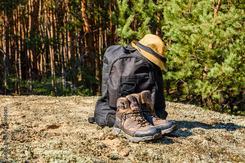 Backpack, touristic boots and hat on a ground in a coniferous forest