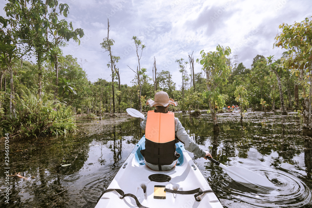Obraz premium woman kayaker kayaking on river in forest on cloudy day