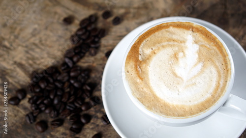 Cappuccino or latte art coffee. Free hand pouring some foam of milk on top. A white ceramic cup on the wood table with some coffee beans. The best food and drink in the world. Fresh energy everyday.