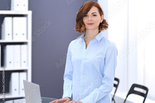 Young brunette business woman looks like a student girl working in office. Caucasian girl standing straight