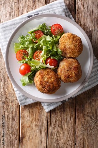 Tasty Danish pork minced meat patties in breading with fresh vegetable salad close-up on the table. Vertical top view