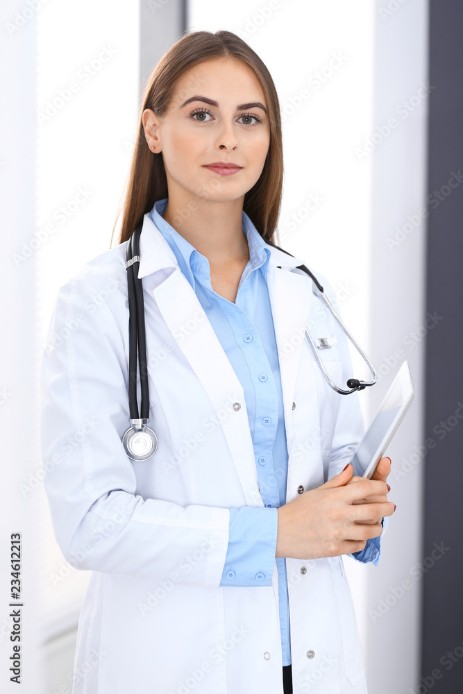 Doctor woman using tablet computer while standing straight near window in hospital. Happy physician at work. Medicine and health care concept Doctor woman using tablet computer while standing straight near window in hospital. Happy physician at work. Medicine and health care concept