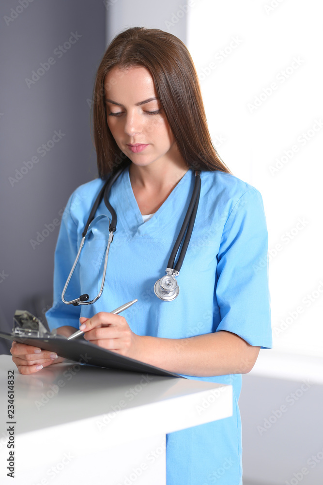 Doctor woman at work. Portrait of female physician filling up medical form while standing near reception desk at clinic or emergency hospital. Medicine and healthcare concept Doctor woman at work. Portrait of female physician filling up medical form while standing near reception desk at clinic or emergency hospital. Medicine and healthcare concept