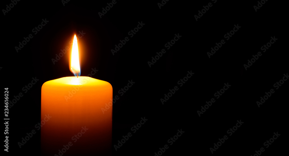 One orange candle flame burning in darkness on black background with copy space for text. One orange candle flame burning in darkness on black background with copy space for text.
