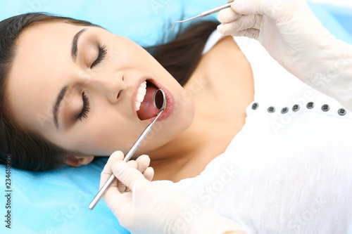 Young female patient visiting dentist office.Beautiful woman with healthy straight white teeth sitting at dental chair with open mouth during oral checkup while doctor working at teeth