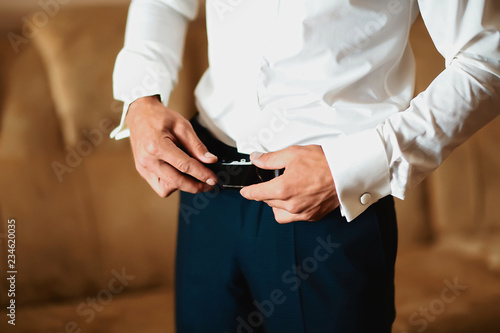 Grooms morning preparation, handsome groom getting dressed and preparing for the wedding, wearing a belt