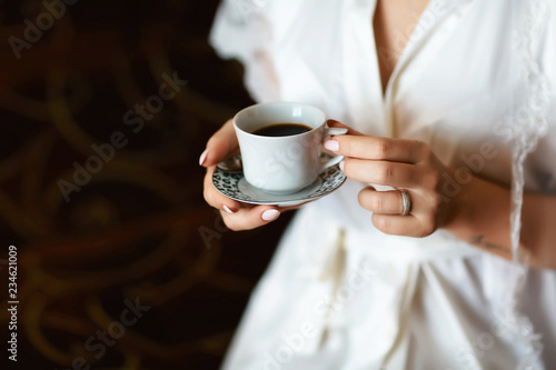 A bride s morning  coffee for breakfast  transparent white peignoir and gentle hands. A picture of an elegant female hand with fine manicure pulling to a perfect cup of coffee