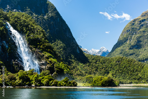 Waterfall in the  Milford Sound, Fiordland National Park, New Zealand. Lushgreen hills, waterfall  on the left side of the photo,  water perspective photo