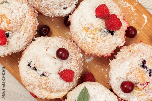 Homemade fruit muffins sprinkled with powdered sugar on board.