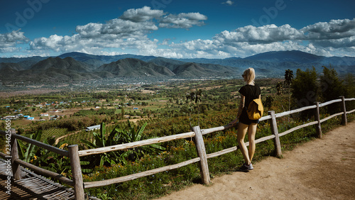 Modern girl with tattoos looks from above a beautiful view of the city of Pai. She is wearing a backpack and denim shorts. Asia travel © Artem Markin