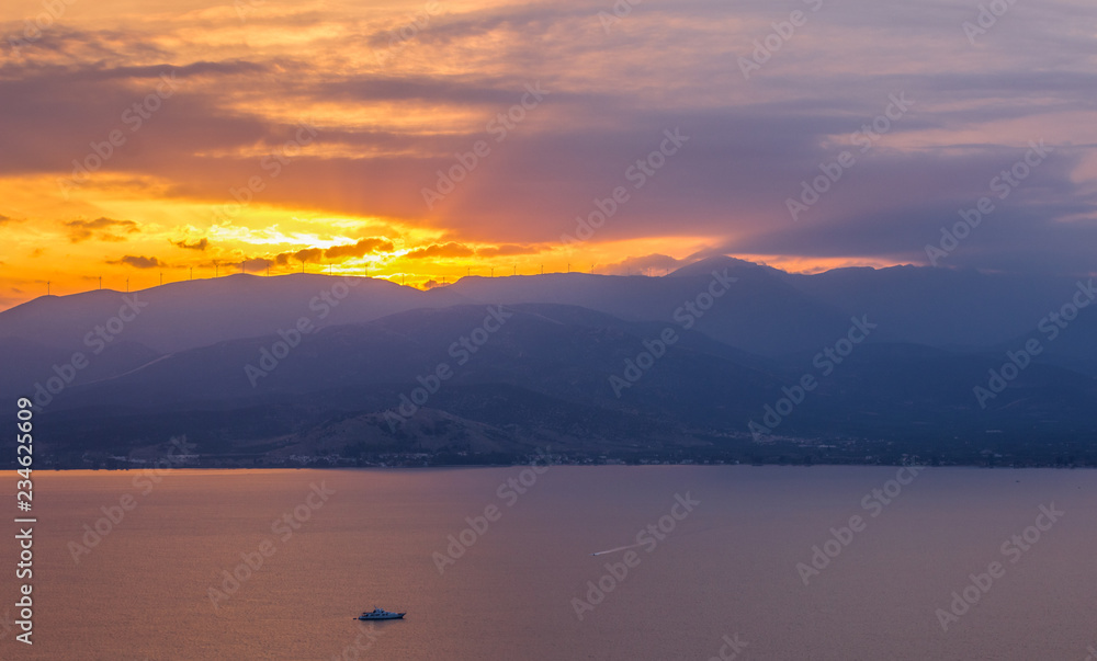 beautiful dramatic nature scenery landscape of mountain horizon background silhouette and sea bay with one small ship in romantic sunset evening twilight time with sun rays from ridge 