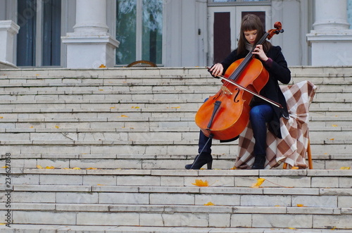 young woman playing cello on the steps of marble staircase of an ancient house