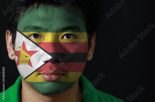 Portrait of a man with the flag of the Zimbabwe painted on his face on black background. The concept of sport or nationalism.