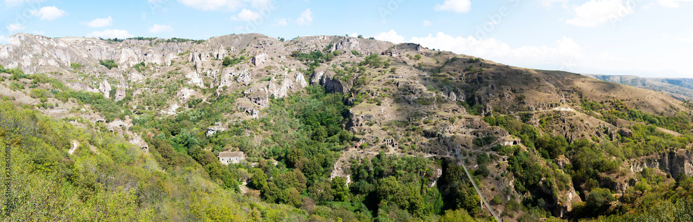 Fototapeta premium Panorama beautiful canyon at Khndzoresk cave settlement (13th-century, used to be inhabited till the 1950s) with a suspension bridge underneath, Syunik region, Armenia