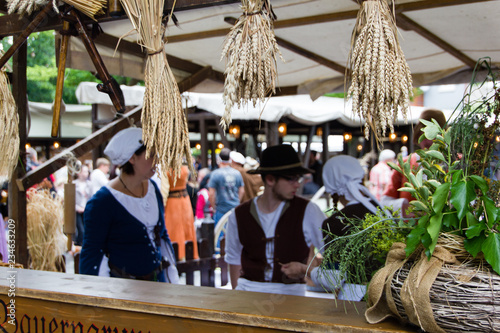 Scene with wheat hanging from the top at a counter and blurry people dressed in medieval clothes behind. Selective focus