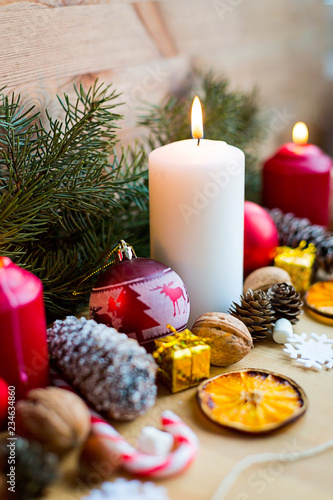 Christmas lighted candles decorated with fir tree and cones on wooden background