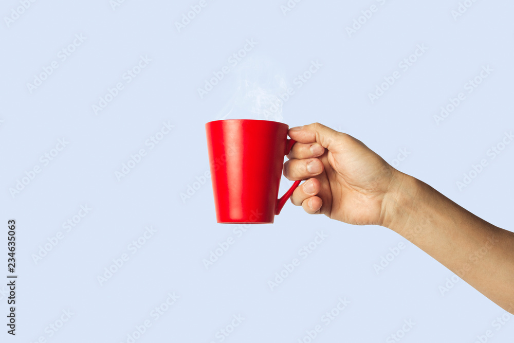 Obraz premium Female hand holding a red cup with hot coffee on a blue background. Side view