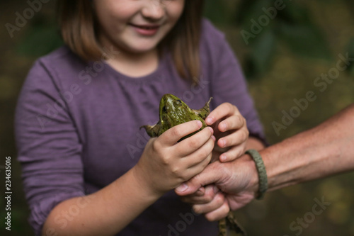 child studies frog, girl holds big frog in hands