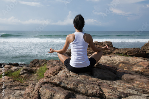 Yoga woman clothing in white meditation at the seaside cliff edge