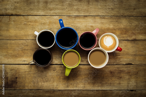 A lot of multicolored cups with coffee and coffee drinks on a wooden background. Concept breakfast with coffee, coffee with friends. Flat lay, top view