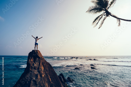 Freedom young woman outstretched arms on seaside rock cliff edge