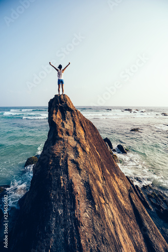 Freedom young woman outstretched arms on seaside rock cliff edge