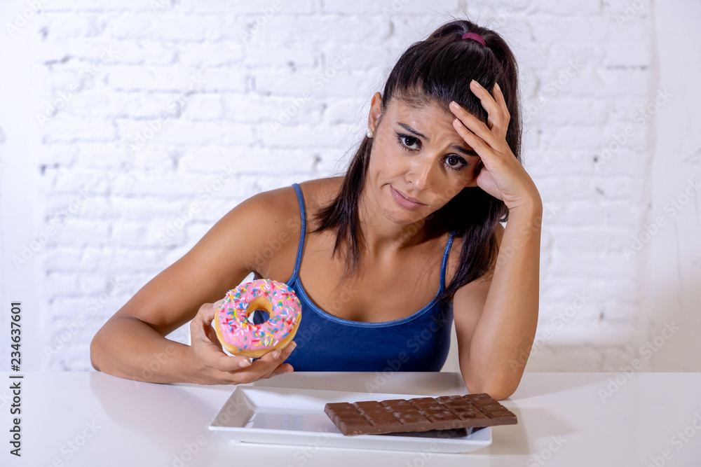 Pretty latin woman looking at chocolate and donuts tired of diet restrictions Pretty latin woman looking at chocolate and donuts tired of diet restrictions