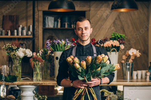 Man florist holding a protea flowers arrangements in modern interior floral shop. Small business, welcoming concept. photo