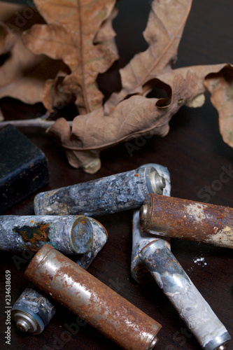 Spent batteries, coated with corrosion. Different shapes and sizes. They lie on a dark background among the dead autumn leaves. Environmental protection, recycling.